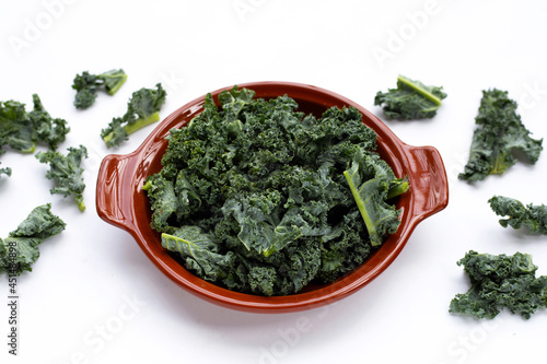 Kale leaves in brown bowl on white background.