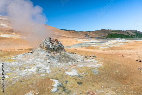 Steaming fumarole in a geothermal area on a clear summer day. A winding road is visible in background. Hverir, Iceland.