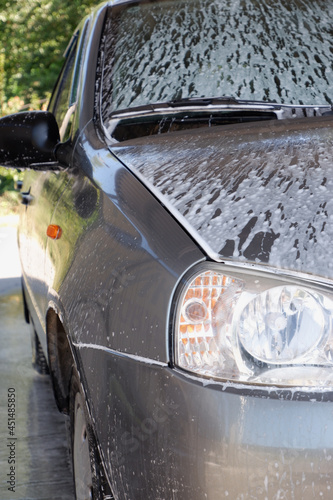 Car wash with a pressure washer. The side of the car is covered with foam.