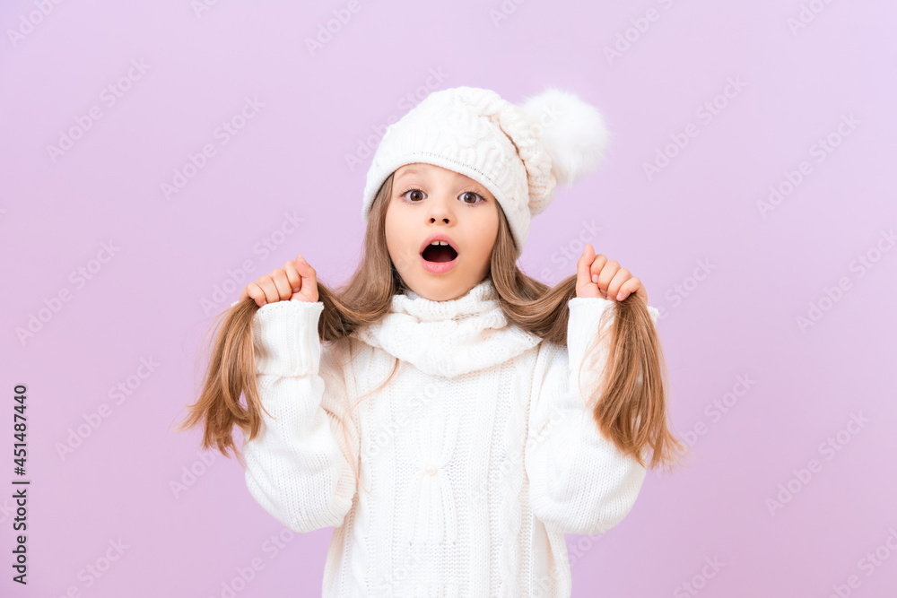 A schoolgirl in a winter hat holds her hair with her hands and opened her mouth in surprise. A schoolgirl in a winter hat holds her hair with her hands and opened her mouth in surprise.