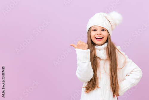 A little girl in a winter sweater and hat points to your ad on an isolated pink background.
