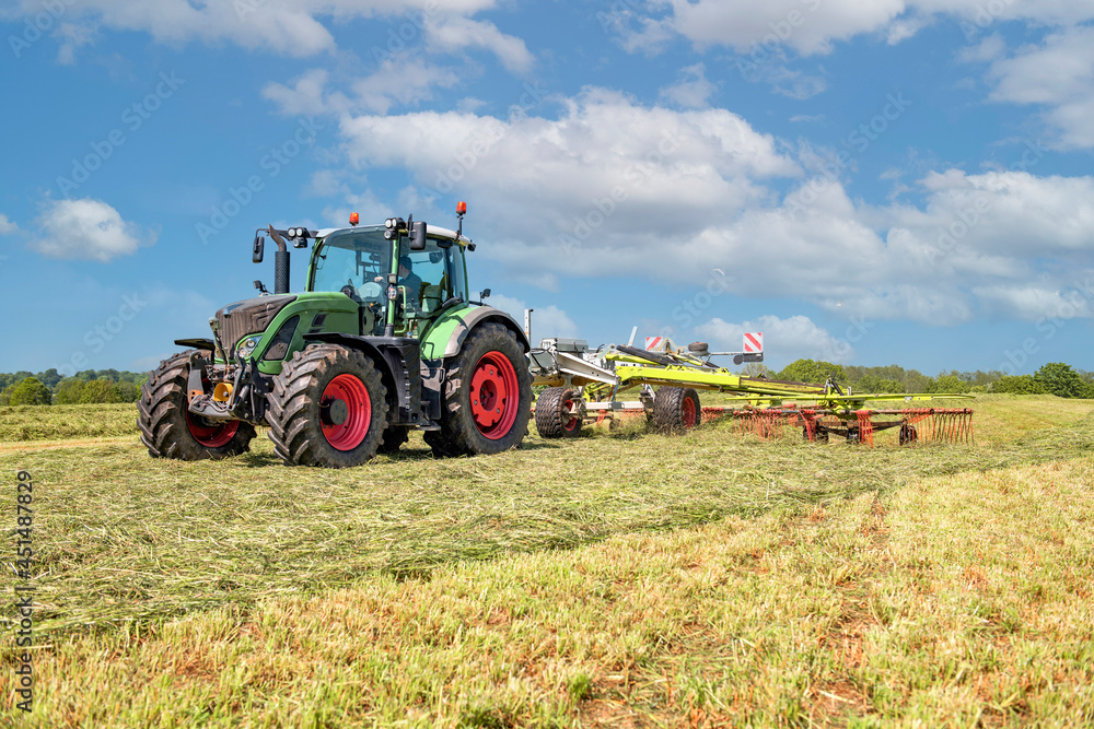 A Tractor with hay tedder turning the grass cuttings in the meadow A Tractor with hay tedder turning the grass cuttings in the meadow