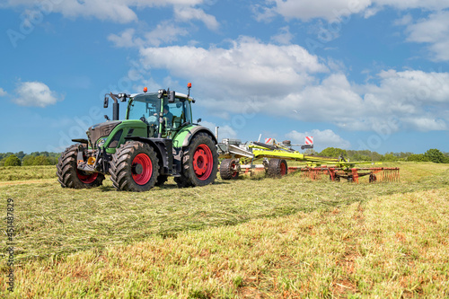 A Tractor with hay tedder turning the grass cuttings in the meadow photo