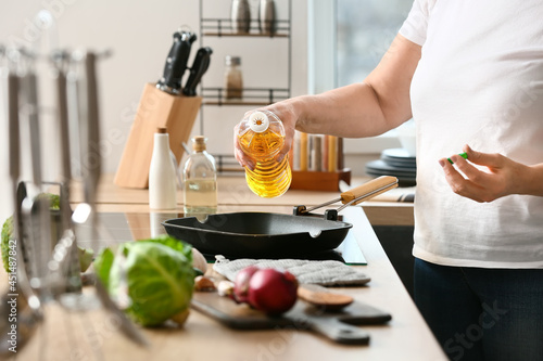 Fotografi Mature woman pouring oil into frying pan in kitchen