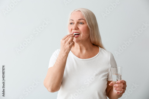 Mature woman taking fish oil on light background