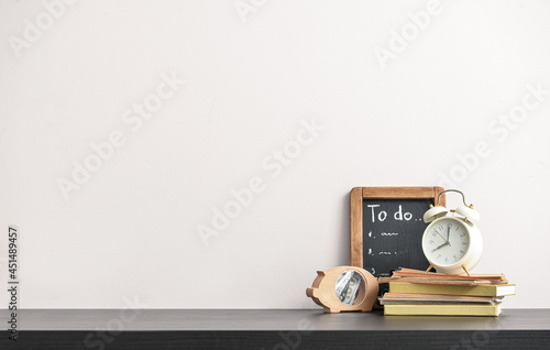 Stylish workplace with to-do list and alarm clock near light wall photo