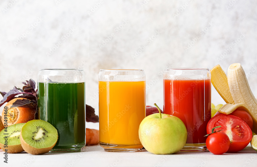 Glasses with healthy juice, fruits and vegetables on light background Glasses with healthy juice, fruits and vegetables on light background