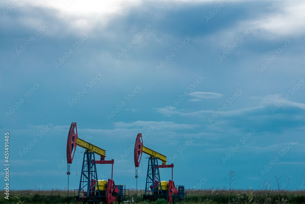 pumpjacks operating at an oil well in field under cloudy sky pumpjacks operating at an oil well in field under cloudy sky