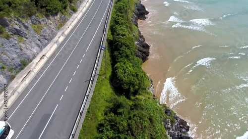 Aerial flight with drone above the road when passing vehicles. On the Oriñón beach in Cantabria, Spain