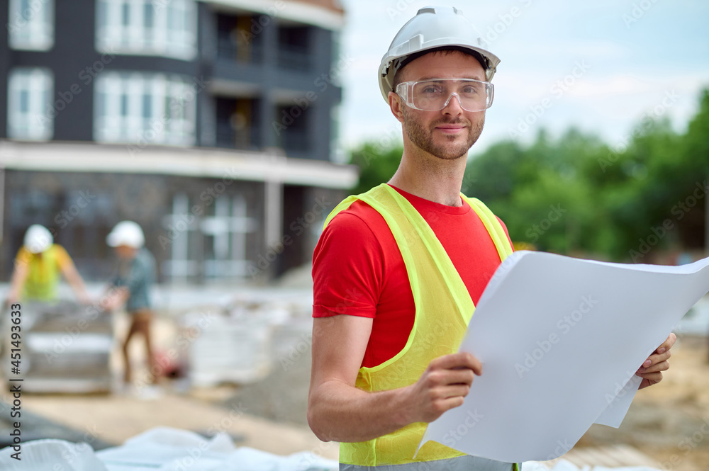 Architect in a hardhat and protective eyewear holding his drawings Architect in a hardhat and protective eyewear holding his drawings
