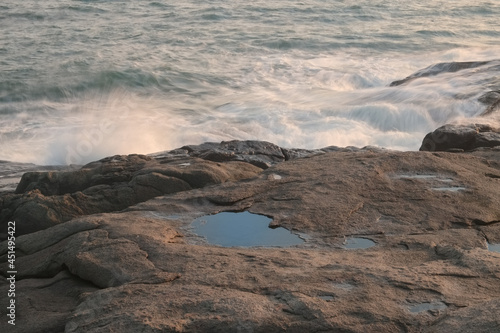 A calm tranquil pool of water stuck between rocks with the rough ocean waves in the background