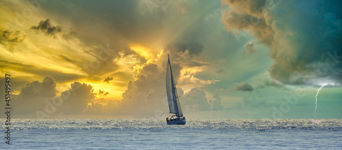 Canvas Print Sailboat navigating a silvery sea in a stormy cloudy sunset