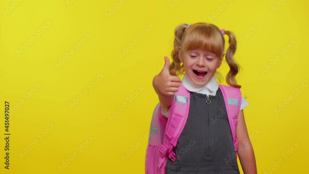 Smiling cute schoolgirl kid child looking at copy space for promotional content holding hand, wears pink backpack and white t-shirt, standing isolated on yellow studio background. Education, school Smiling cute schoolgirl kid child looking at copy space for promotional content holding hand, wears pink backpack and white t-shirt, standing isolated on yellow studio background. Education, school