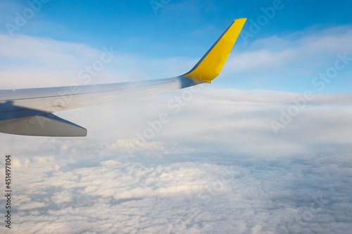 Wing of airplane flying above the clouds in the blue sky