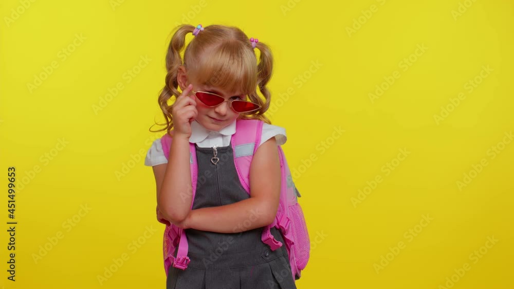 Playful happy teen child kid schoolgirl in uniform, sunglasses blinking eye, looking at camera with toothy smile, winking and flirting, expressing optimism on yellow studio background. Back to school Playful happy teen child kid schoolgirl in uniform, sunglasses blinking eye, looking at camera with toothy smile, winking and flirting, expressing optimism on yellow studio background. Back to school