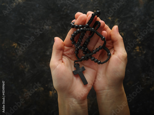 In women's hands, a crucifix and a rosary. Minimalism. Dark background. Religion, faith, Catholicism, prayer, meditation. Poster, banner, advertisement.