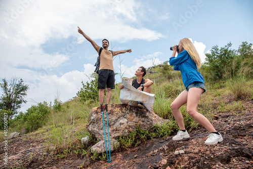 man stands on a rock and a man looks at a road map and a woman takes a picture
