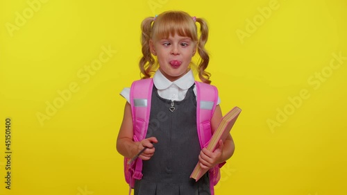 Smiling cute funny girl in school uniform, making humorous face with eyes crossed, playing fool, having fun with stupid brainless dumb expression over yellow studio background. Back to school concept photo