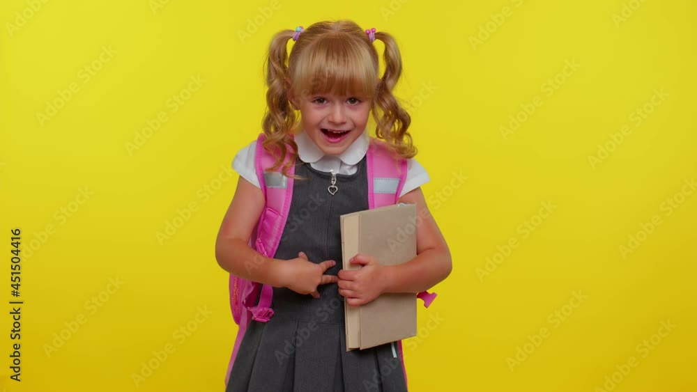 Happy little blond teenage student girl kid in school uniform celebrate success win scream rejoices doing winner hands gesture say Yes. Yellow studio wall background. Education, back to school, study Happy little blond teenage student girl kid in school uniform celebrate success win scream rejoices doing winner hands gesture say Yes. Yellow studio wall background. Education, back to school, study