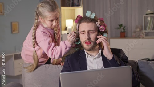 parent works remotely in home office while female child applies makeup while sitting in isolation due to pandemic photo