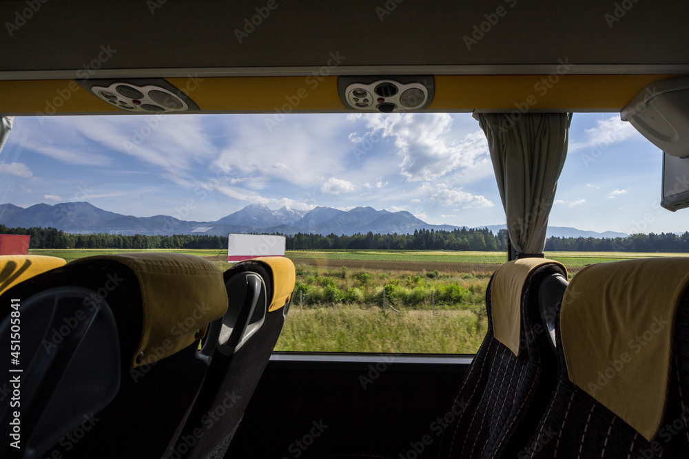 Large window in an empty bus with modern seats with the slovenian mountains of the Julian alps in background, taken from a motorway, in a moder long distance coach bus...