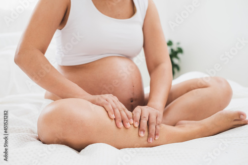 Asian pregnant woman with big belly has legs ache, pain massaging her legs on bed