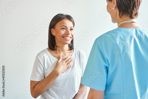 Thank you for help. Happy grateful african american young woman patient thanking professional female doctor for consultation, with hand on chest saying thanks to doc during healthcare visit in clinic