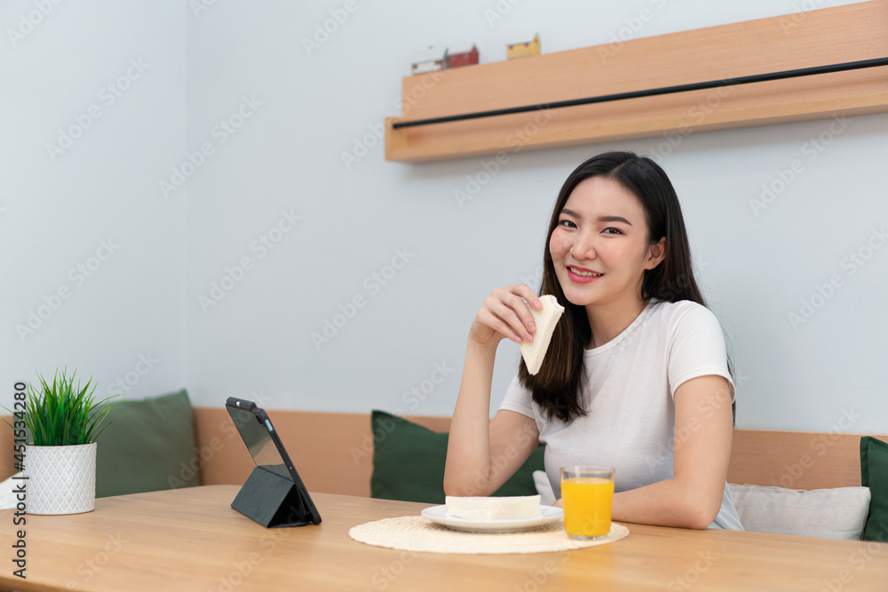 Living room concept a female adult enjoying eating sandwiches and orange juice watching online media in the work break Living room concept a female adult enjoying eating sandwiches and orange juice watching online media in the work break
