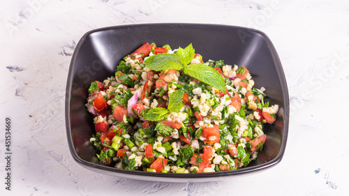 Traditional arabic tabbouleh salad with bulgur in a black bowl on a light background photo