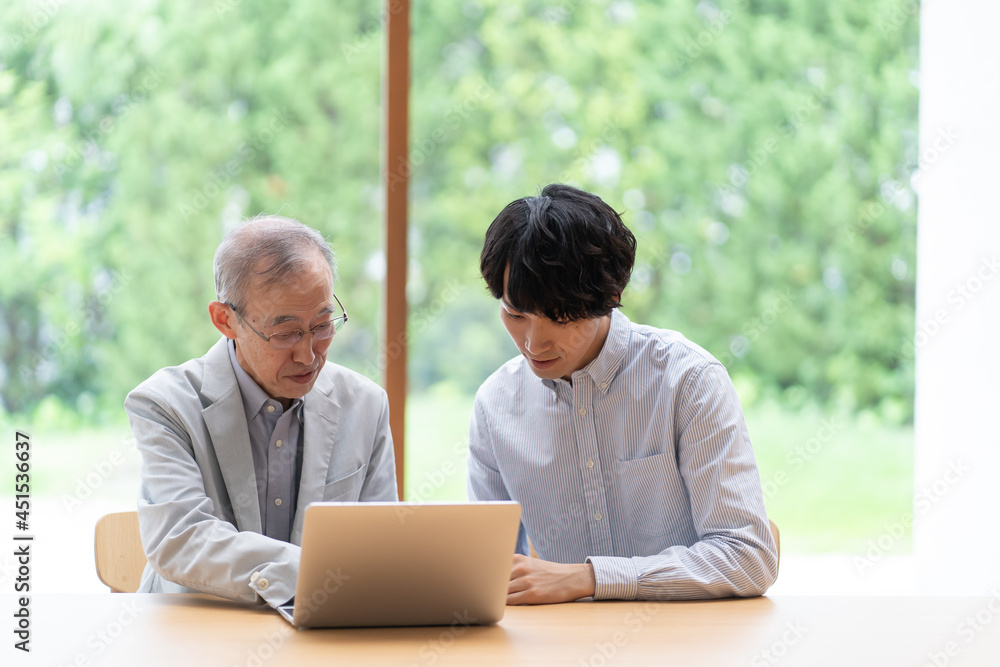 パソコンを見る若い男性とシニア パソコンを見る若い男性とシニア