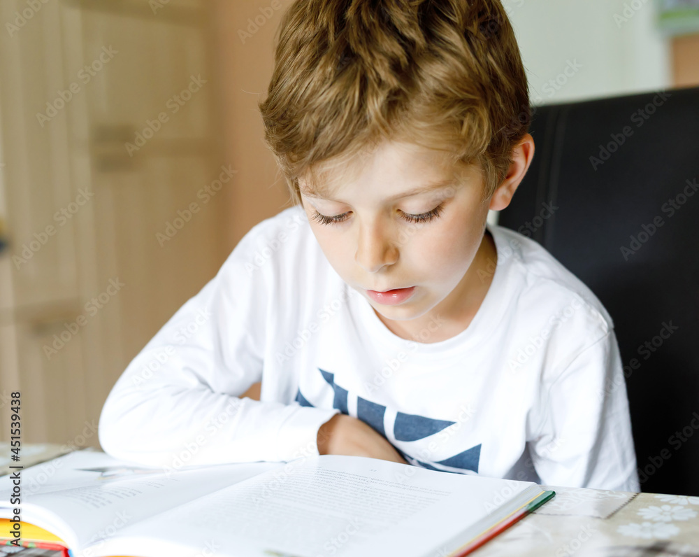 Little blonde school kid boy reading a book at home. Child interested in reading magazine for kids. Leisure for kids, building skills and education concept Little blonde school kid boy reading a book at home. Child interested in reading magazine for kids. Leisure for kids, building skills and education concept