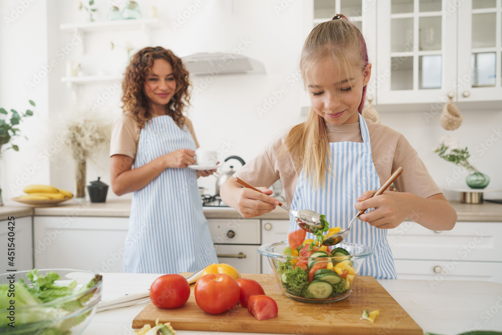 Mommy teaching her teen daughter to cook vegetable salad in kitchen Mommy teaching her teen daughter to cook vegetable salad in kitchen