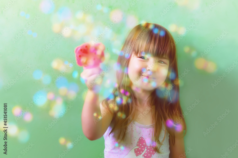 A happy Child is playing with bubbles at home. A photo of a pretty little girl playing with soap bubbles at home. A cute little girl blows bubbles from a cannon. The concept of children's games.