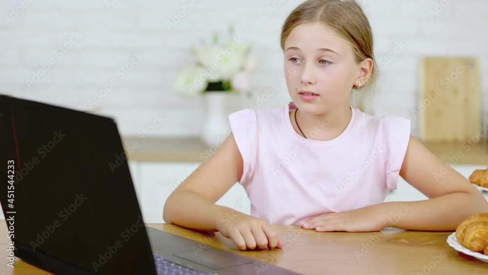 girl looking at a laptop sitting at the table in the kitchen girl looking at a laptop sitting at the table in the kitchen