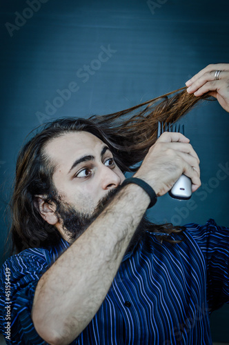 portrait of a young man with a beard and long hair who, with an hair trimmer in his hand, wants to change his look and wants to cut his hair, concept to illustrate the desire to change photo