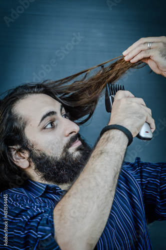 portrait of a young man with a beard and long hair who, with an hair trimmer in his hand, wants to change his look and wants to cut his hair, concept to illustrate the desire to change photo