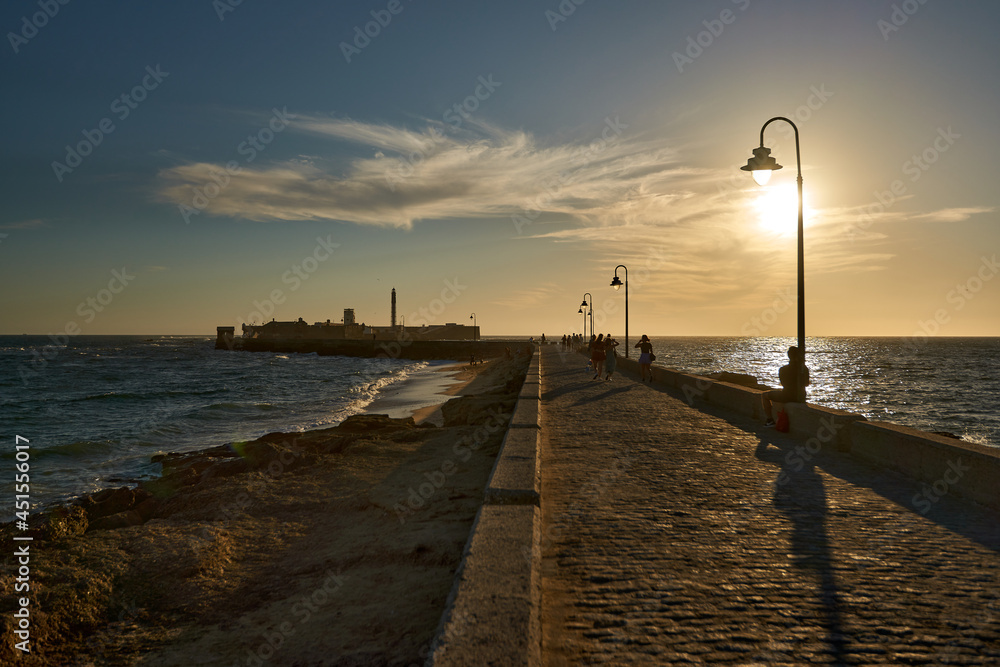 Backlight at sunset on a stone walkway that goes out to sea towards a fortress