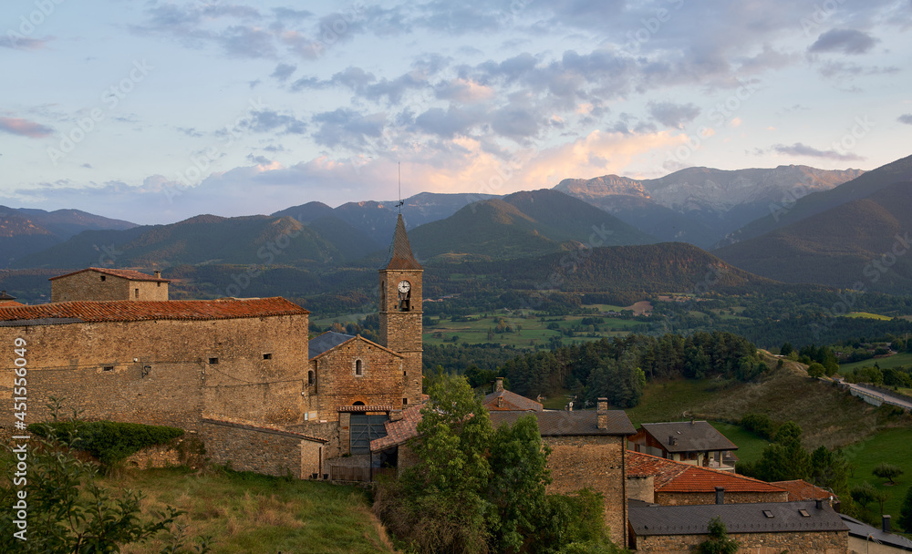 Sunset in the mountains with a green meadow and an old bell tower
