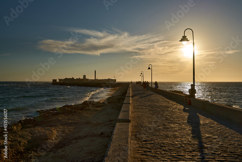 Backlight at sunset on a stone walkway that goes out to sea towards a fortress