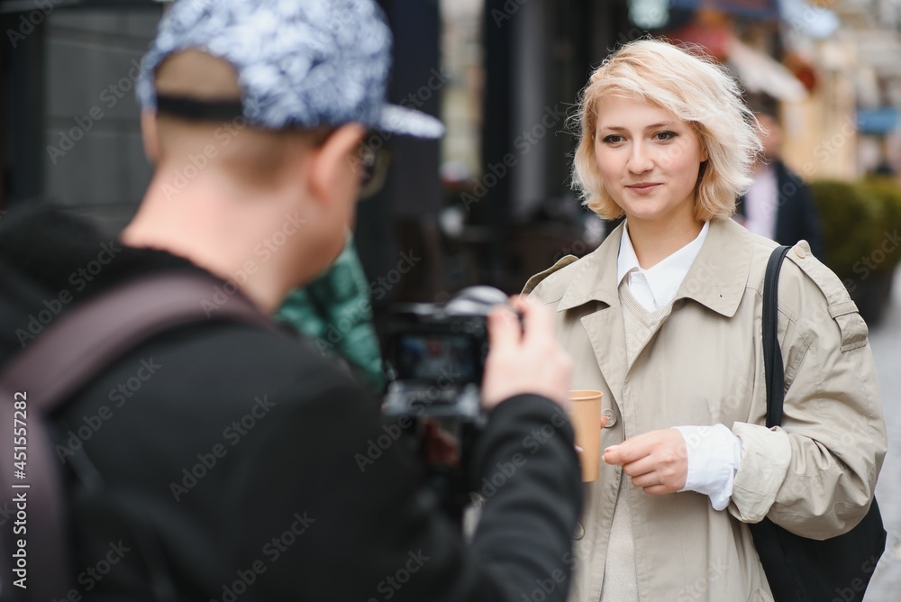 A girl makes a video blog with a cameraman on the street. Young woman blogger, journalist filming with a professional camera and videographer. A girl makes a video blog with a cameraman on the street. Young woman blogger, journalist filming with a professional camera and videographer.