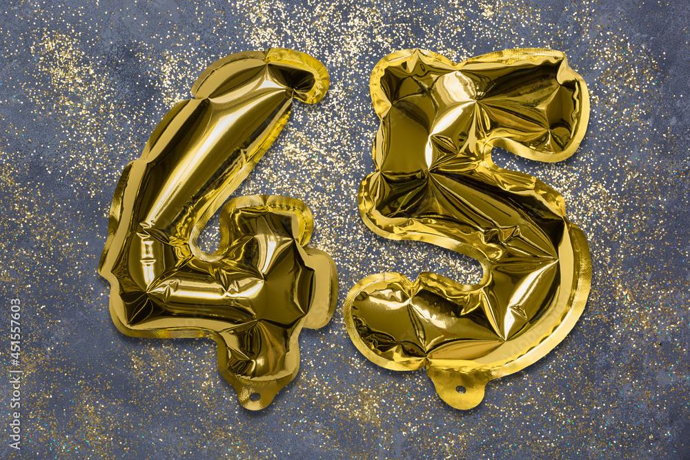 The number of the balloon made of golden foil, the number forty-five on a gray background with sequins. Birthday greeting card with inscription 45. Anniversary concept. Celebration event. The number of the balloon made of golden foil, the number forty-five on a gray background with sequins. Birthday greeting card with inscription 45. Anniversary concept. Celebration event.