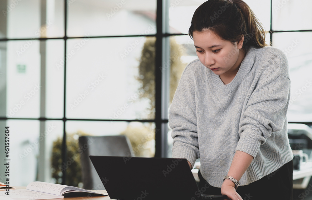A teenage girl looks down at the laptop screen on the table. A teenage girl looks down at the laptop screen on the table.