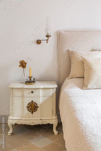 Interior of cozy house in retro style. Classic bedroom with candle and flowers on wooden bedside table near comfortable bed.