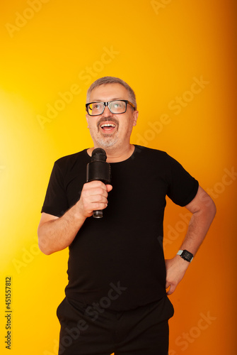 Full profile photo of crazy hipster standing with microphone, music lover singing favorite song, black t-shirts, pants, isolated yellow background color