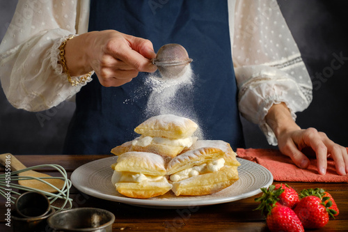 Obraz na plátně powdered icing sugar sprinkling from a sieve in woman's hand, cooking sweet puff