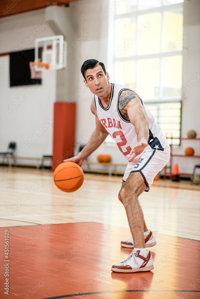 Dark-haired athletic man playing basket-ball in the gym Dark-haired athletic man playing basket-ball in the gym
