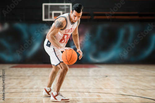 Young athletic man in white sportwear playing basket-ball in the gym