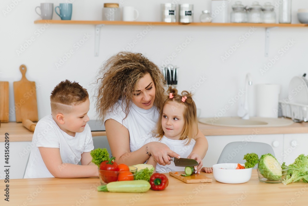 Young mother and her two kids making vegetable salad Young mother and her two kids making vegetable salad