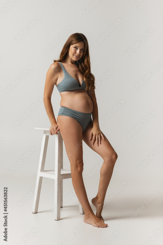 Portrait of happy beautiful pregnant woman in lingerie isolated over grey studio background. Natural beauty, happy motherhood, femininity concept.