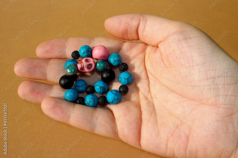 a woman's bracelet made of natural stones of turquoise howlite, onyx, black lava and two pink skulls made of howlite lies in a woman's hand on a brown background. side view a woman's bracelet made of natural stones of turquoise howlite, onyx, black lava and two pink skulls made of howlite lies in a woman's hand on a brown background. side view